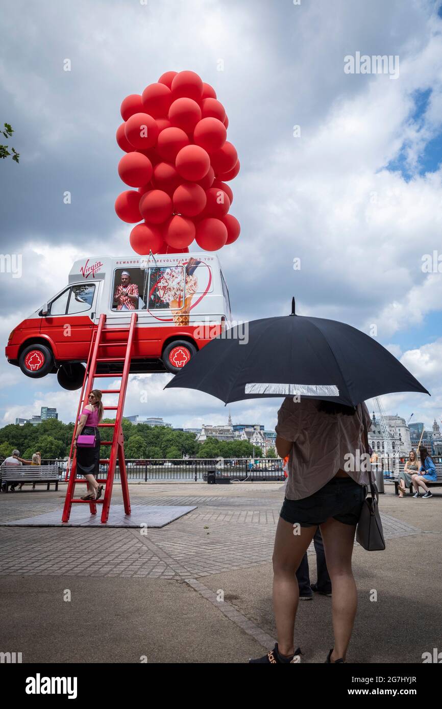 Londra, Regno Unito. 14 luglio 2021. I passanti sulla South Bank si vedono un pulmino gelato che sembra essere portato in alto da palloncini rossi. Lo stunt di Virgin Red sta promuovendo un nuovo programma fedeltà per i clienti in coincidenza con l'uscita del Regno Unito dal blocco il 19 luglio. Credit: Stephen Chung / Alamy Live News Foto Stock