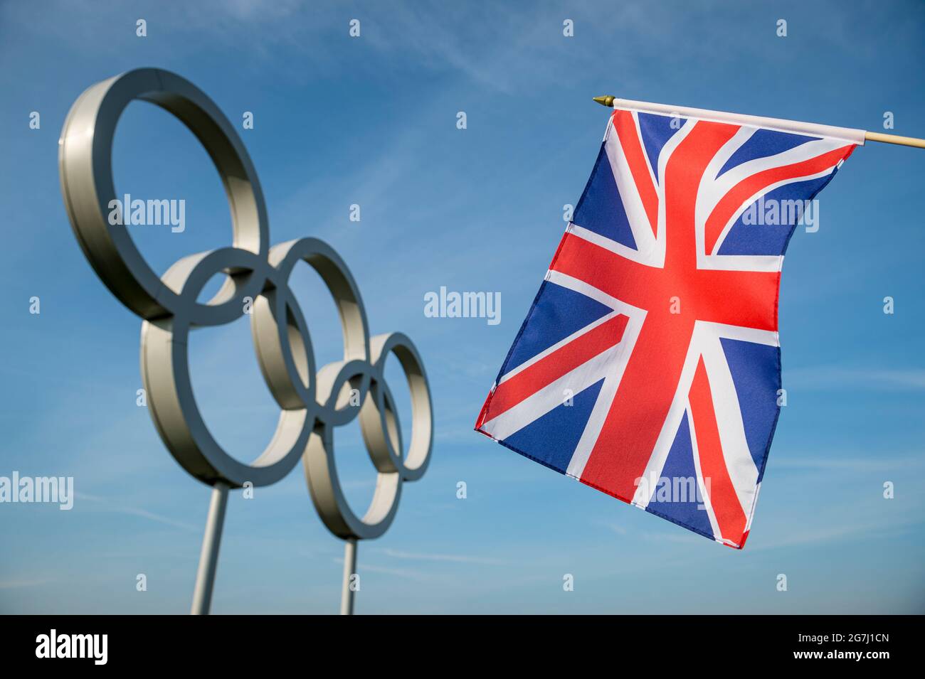 RIO DE JANEIRO - MARZO, 2016: Bandiera Union Jack appesa davanti a un grande set di brillanti anelli olimpici metallici sotto il cielo blu luminoso. Foto Stock