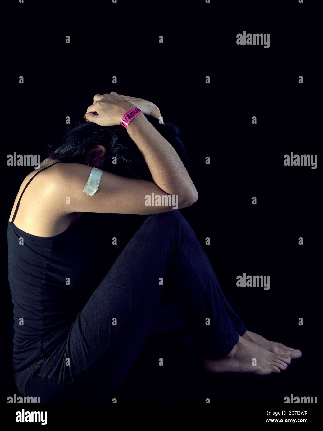 ragazza di brunette angosciata e frustrata seduta nel buio che stringe la testa dopo aver vaccinato covid-19 coronavirus Foto Stock