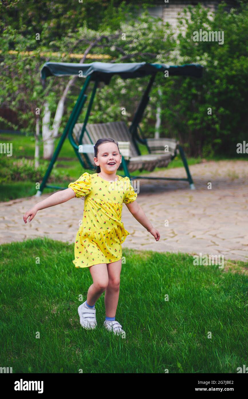 una ragazza ridente balla in un cortile estivo con un'oscillazione giardino sullo sfondo e gode di una giornata calda Foto Stock