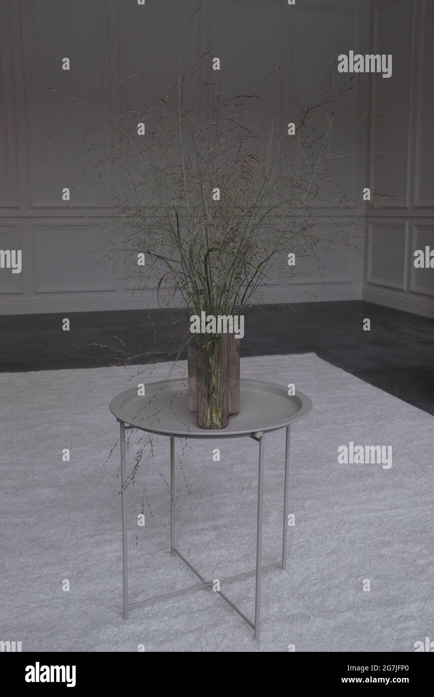 Tavolo in metallo con vaso di fiori con erbe secche su sfondo grigio interno e pareti Foto Stock