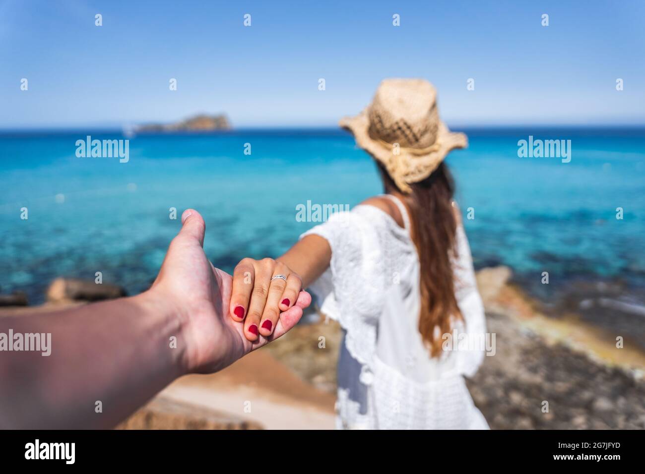 Ragazza con un vestito bianco e cappello marrone che tiene la mano con un  ragazzo su una spiaggia paradiso Foto stock - Alamy
