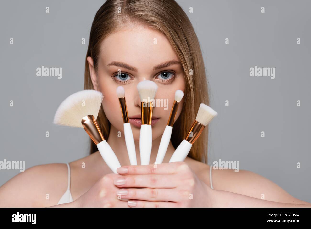 giovane donna che tiene insieme di spazzole cosmetiche diverse isolato su grigio Foto Stock