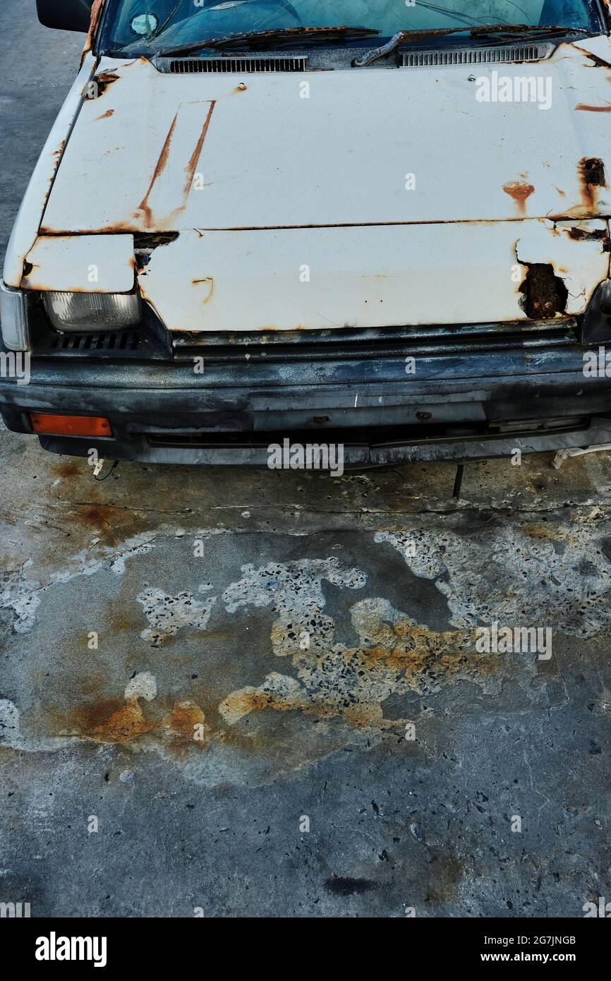 Vecchia auto abbandonata e arrugginita parcheggiata su un pavimento di cemento. Foto Stock