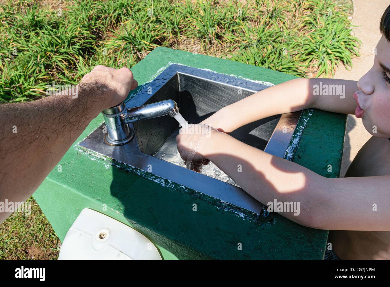 Padre che aiuta suo figlio a lavarsi le mani in un lavello esterno in un parco pubblico. Foto Stock