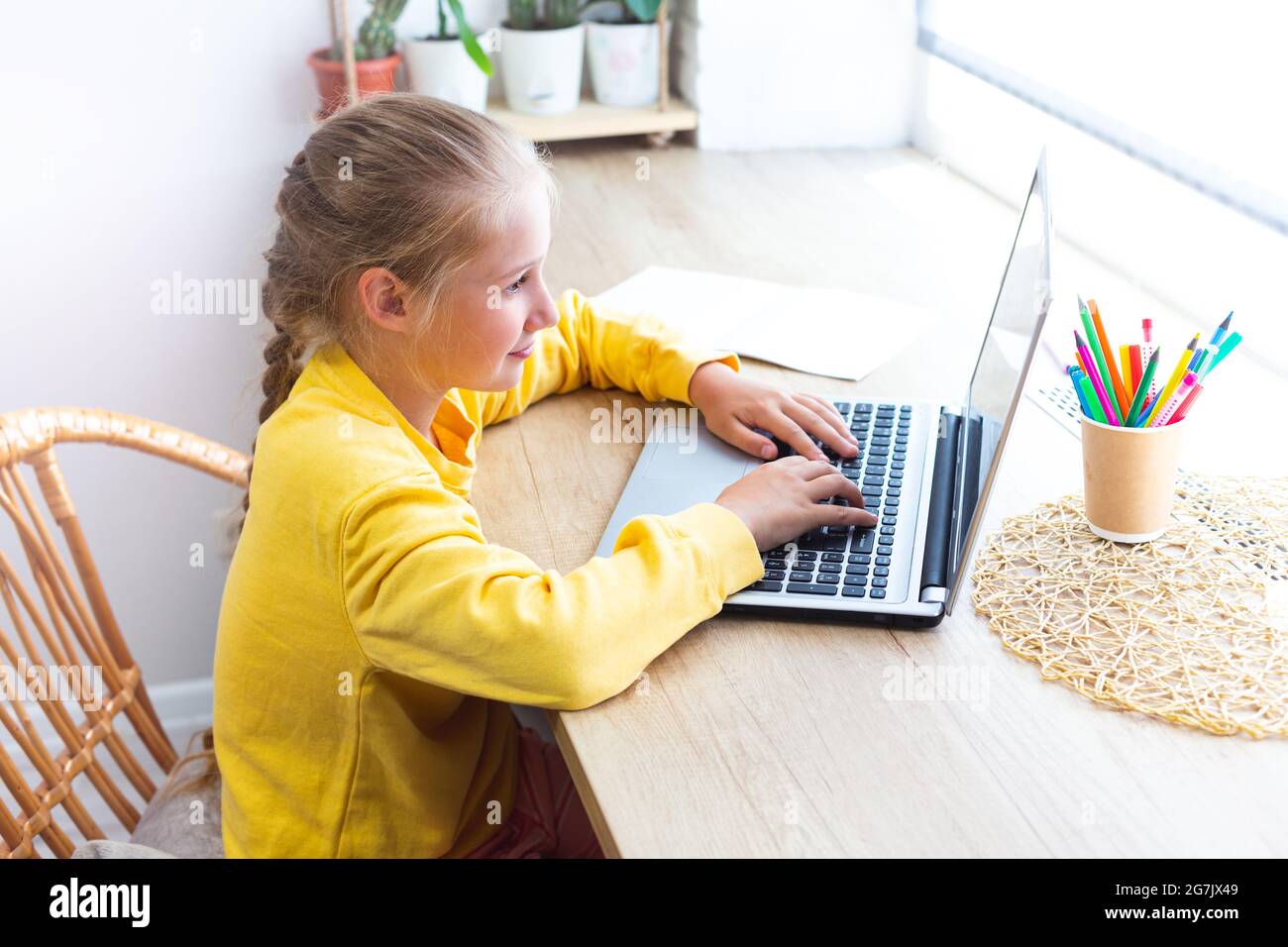 Caucasica bionda scuola ragazza, digitando su una tastiera portatile mentre si siede vicino alla finestra a casa, facendo compiti, blogging, chattando, guardando sociale Foto Stock