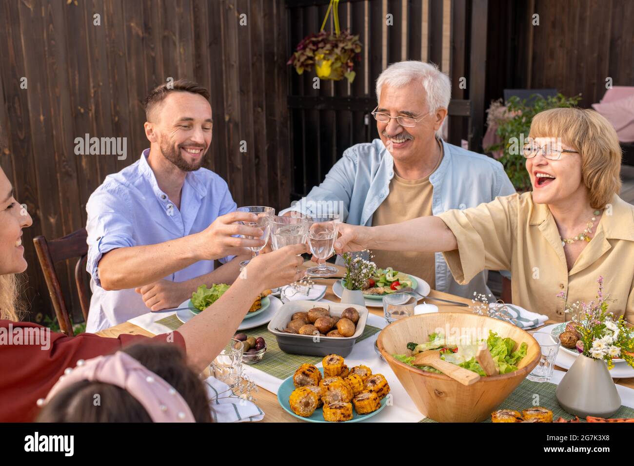 Felice coppia anziana eccitato occhiali da clinking con bevande alcoliche con i loro bambini adulti alla festa di famiglia Foto Stock