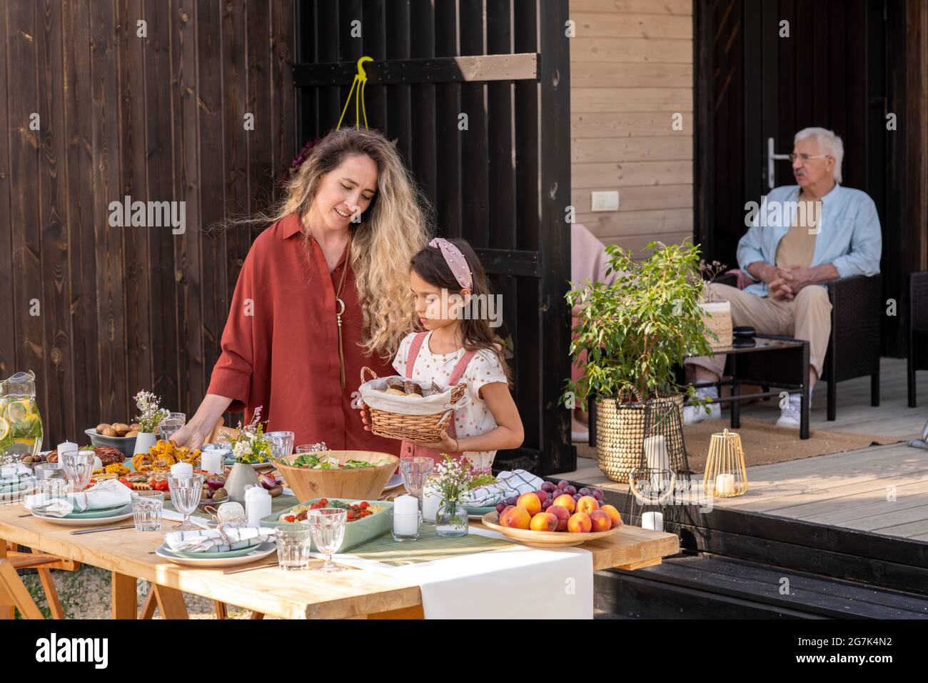 Bella bambina mettendo cestino di pane sul tavolo da pranzo aiutando la sua mamma a servire tavolo per evento di famiglia Foto Stock