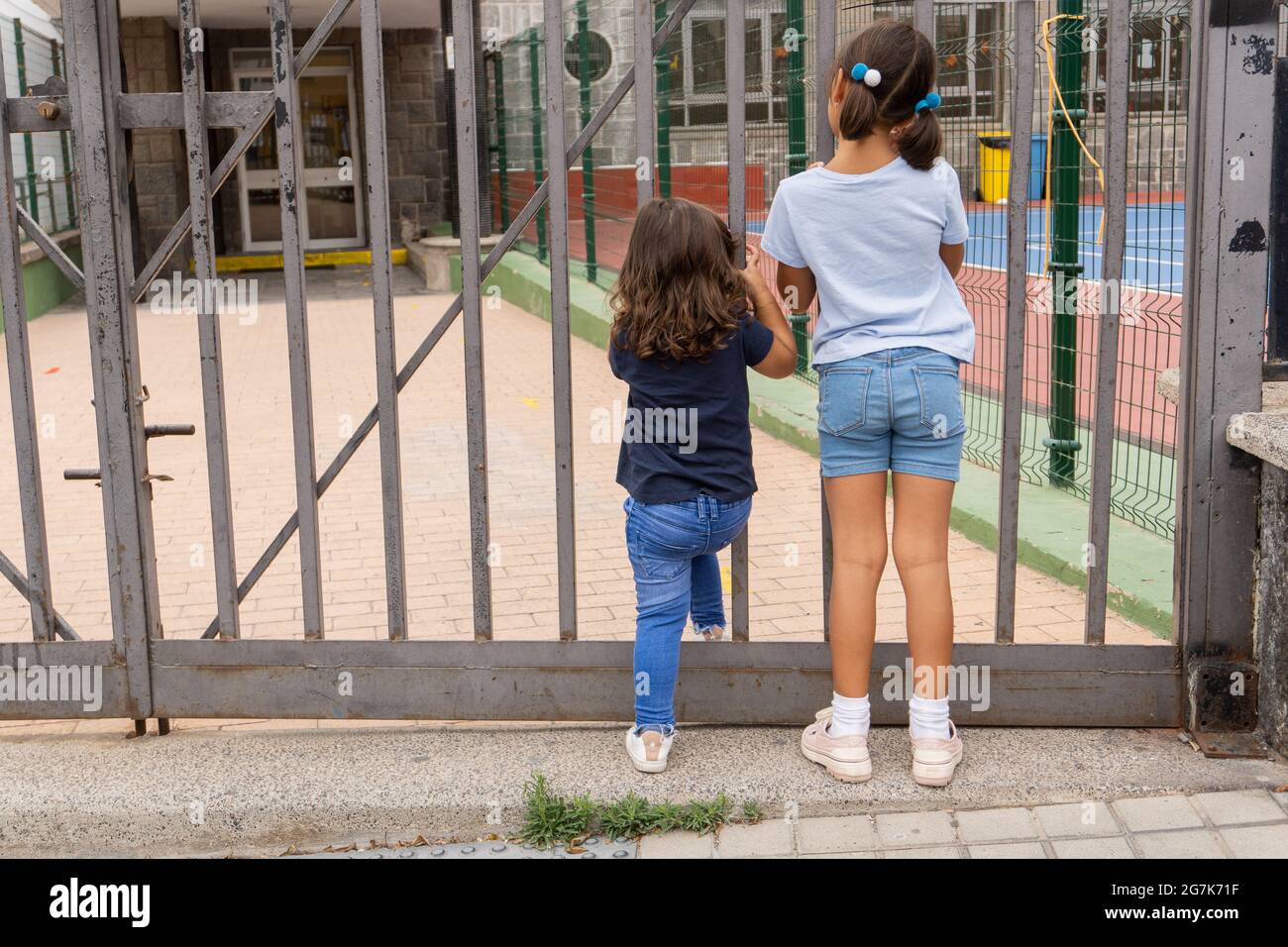 Due ragazze caucasiche di età diversa aspettano alla porta della scuola. Foto Stock