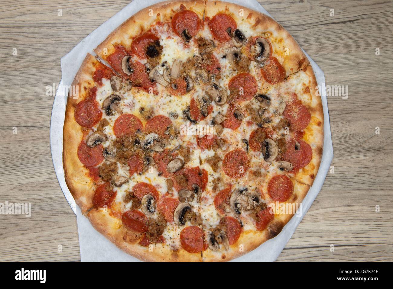 La vista panoramica dei formaggi fusi copre questa pizza a base di funghi e pepperoni con la crosta croccante cotta alla perfezione. Foto Stock