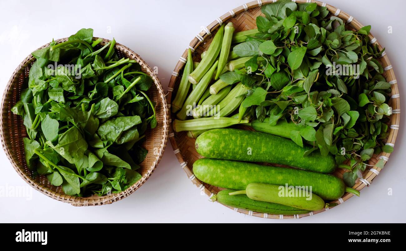 Verdure verdi appena raccolte dal giardino della città sulla casa sul tetto della città di ho chi Minh, frutta di melone, calabash, okra, spinaci sul cesto su sfondo bianco Foto Stock