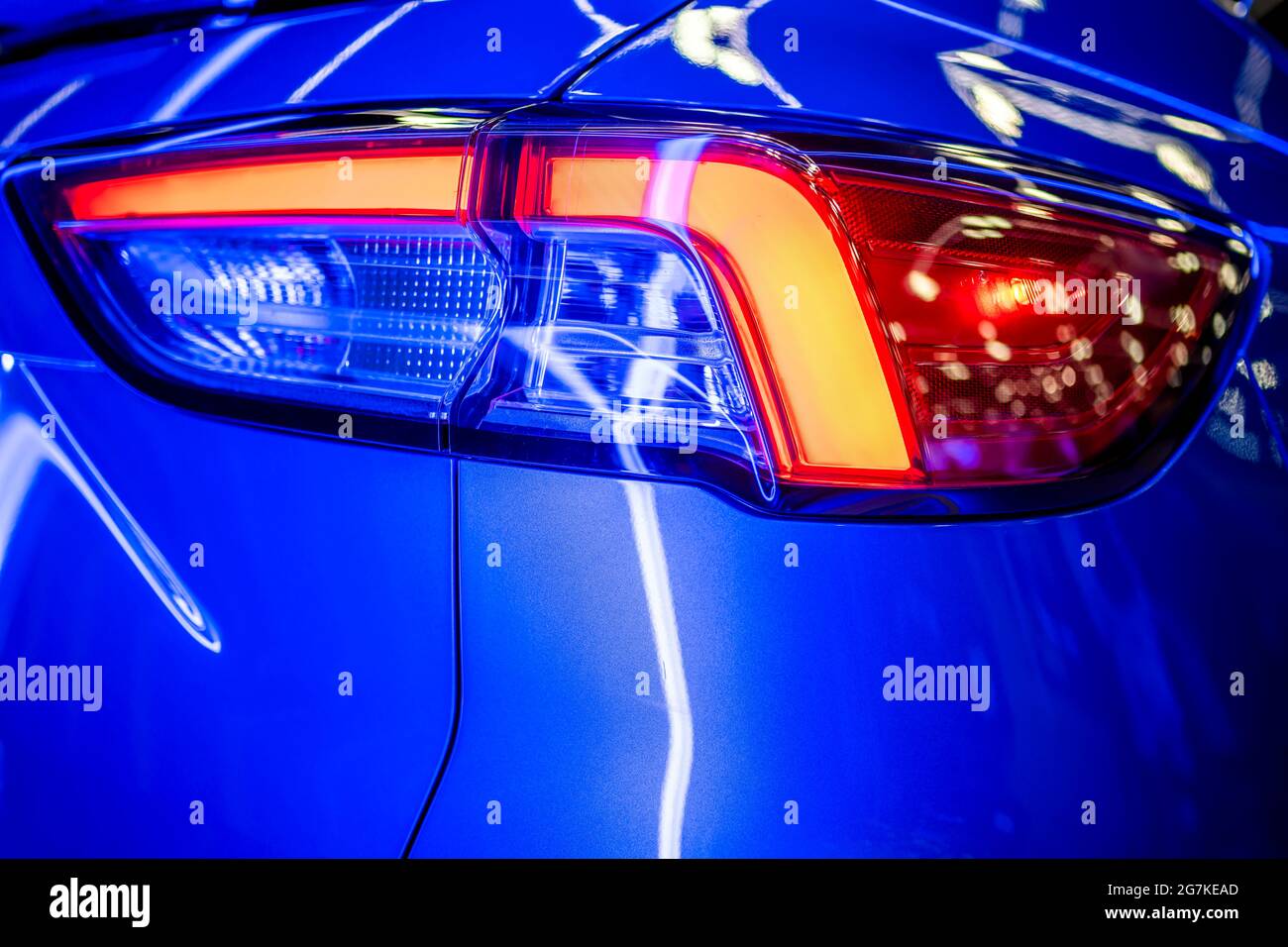 Frammento della luce posteriore in vetro accesa della vettura blu brillante con riflesso di luce al neon e riflesso di oggetti circostanti sul rilievo combinato di Foto Stock
