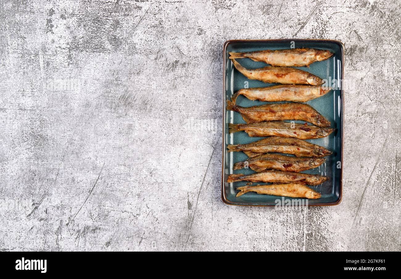 Pan il capelin fritto o il pesce odorato su una piastra rettangolare su uno sfondo grigio scuro. Vista dall'alto, disposizione piatta Foto Stock