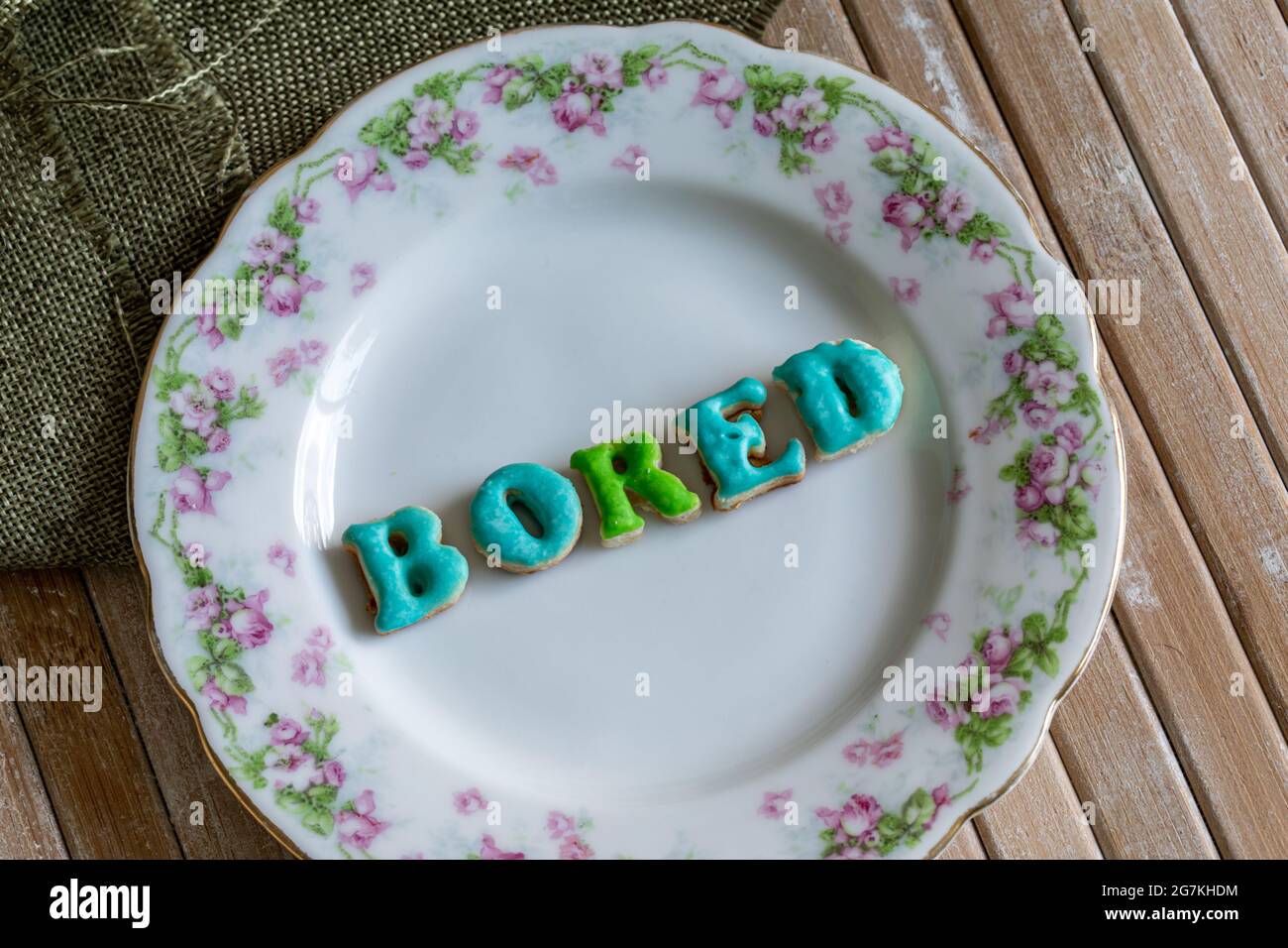 la parola annoiava al centro di un piatto bianco rotondo con motivi floreali intorno su una superficie di legno con luce naturale Foto Stock