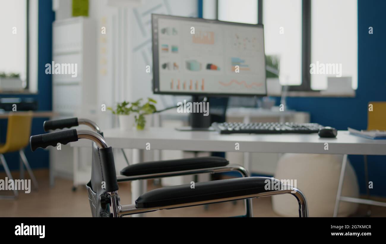Interno di un moderno ufficio finanziario open space senza persone, elegante camera con sedia a rotelle per i lavoratori non validi. Business center con dipendenti paralizzati, spazio di lavoro vuoto, area di lavoro Foto Stock