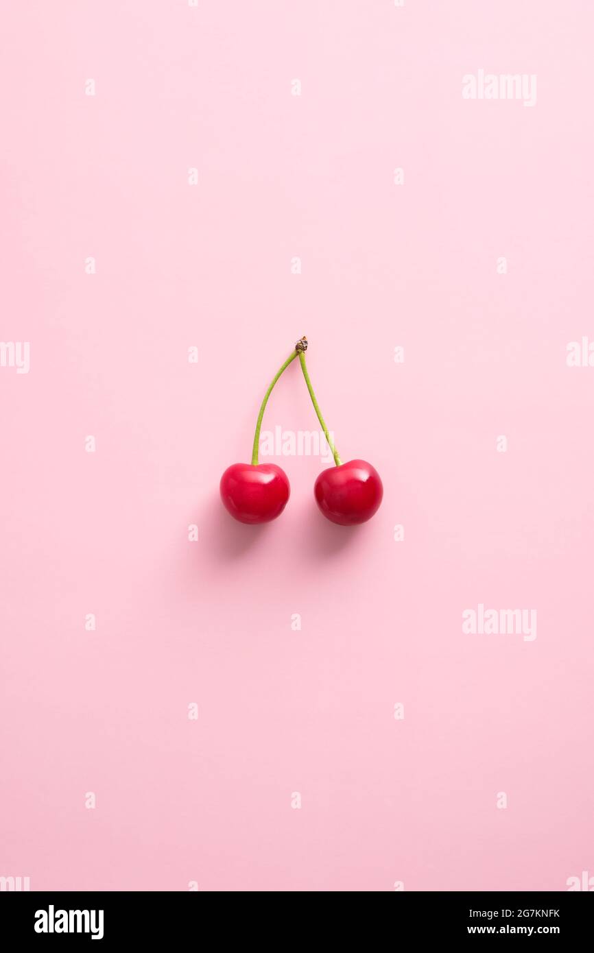Bacche di ciliegia doppio su sfondo rosa. Disposizione piatta, vista dall'alto. Foto Stock