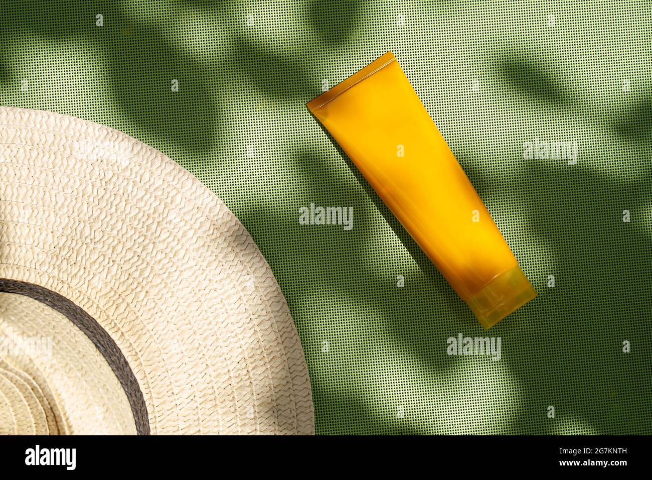 Cappello di rafia piatto e tubo cosmetico arancione su ombreggiature botaniche a trama verde Foto Stock