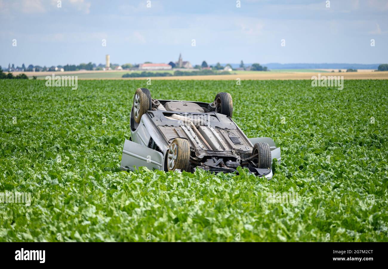 L'auto si è capovolta dopo un incidente in un campo, un tranquillo paesaggio di campagna. Foto Stock