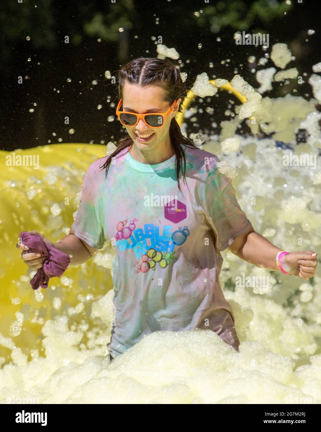 Donna sorridente in occhiali da sole ad un evento benefico Bubble Rush Foam Foto Stock