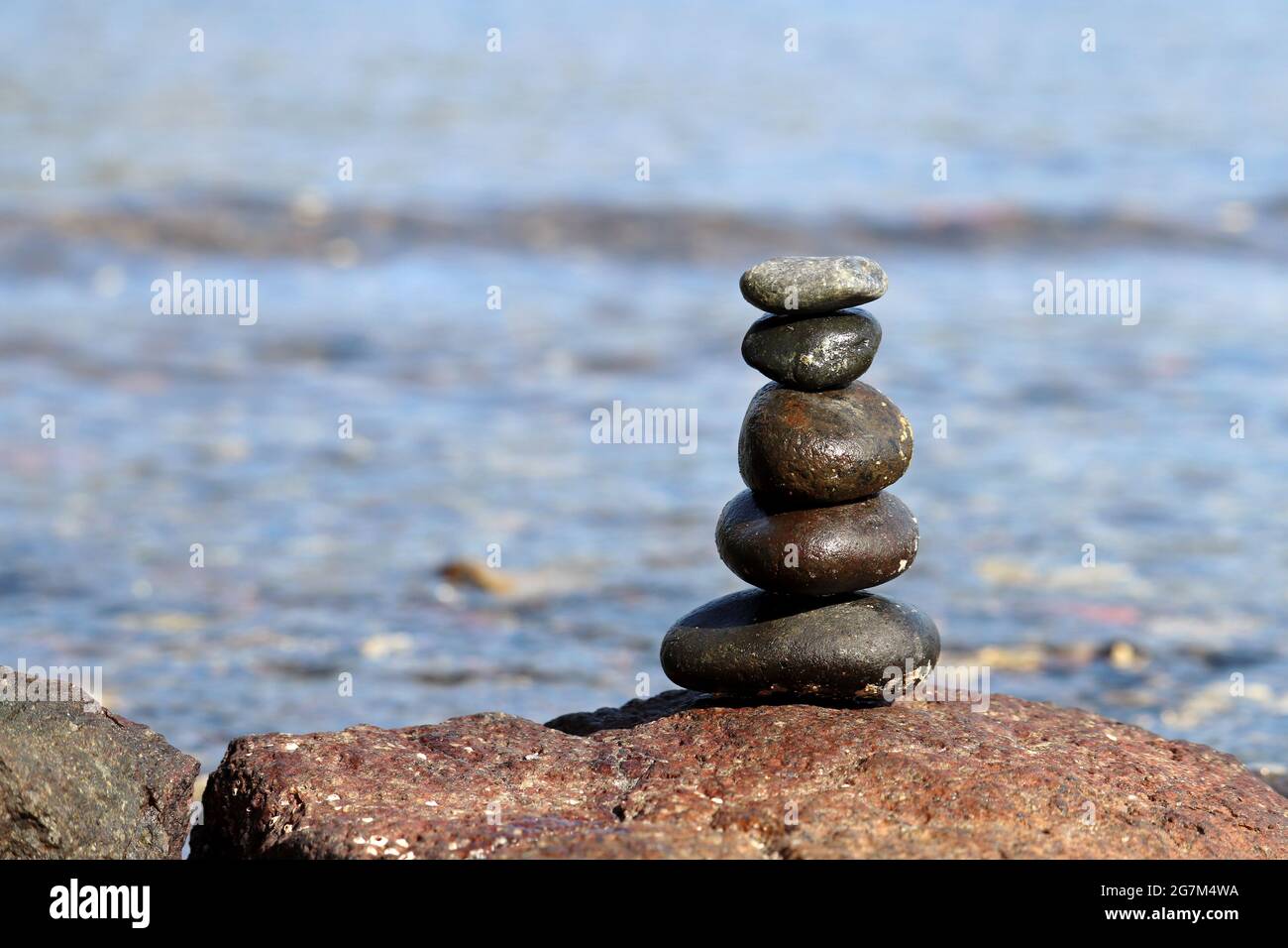 Piramide di ciottoli su sfondo sfocato delle onde del mare. Vacanza estiva, concetto di equilibrio e relax Foto Stock