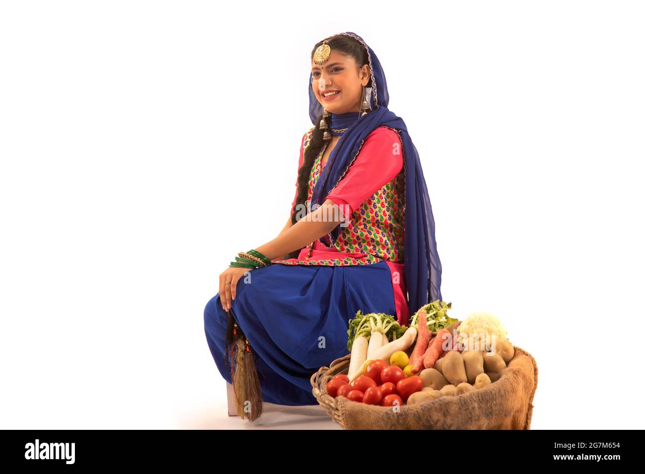 Una donna in costume Giddha seduta con un cesto di verdure al suo fianco. Foto Stock