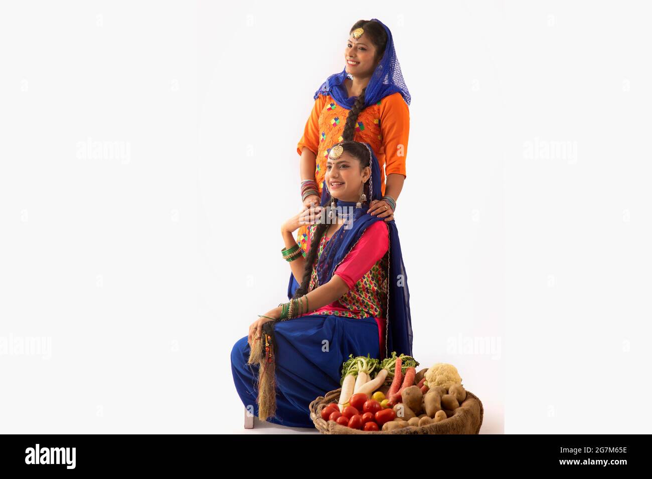 Due donne in costume Giddha insieme con un cesto di verdure al loro fianco. Foto Stock