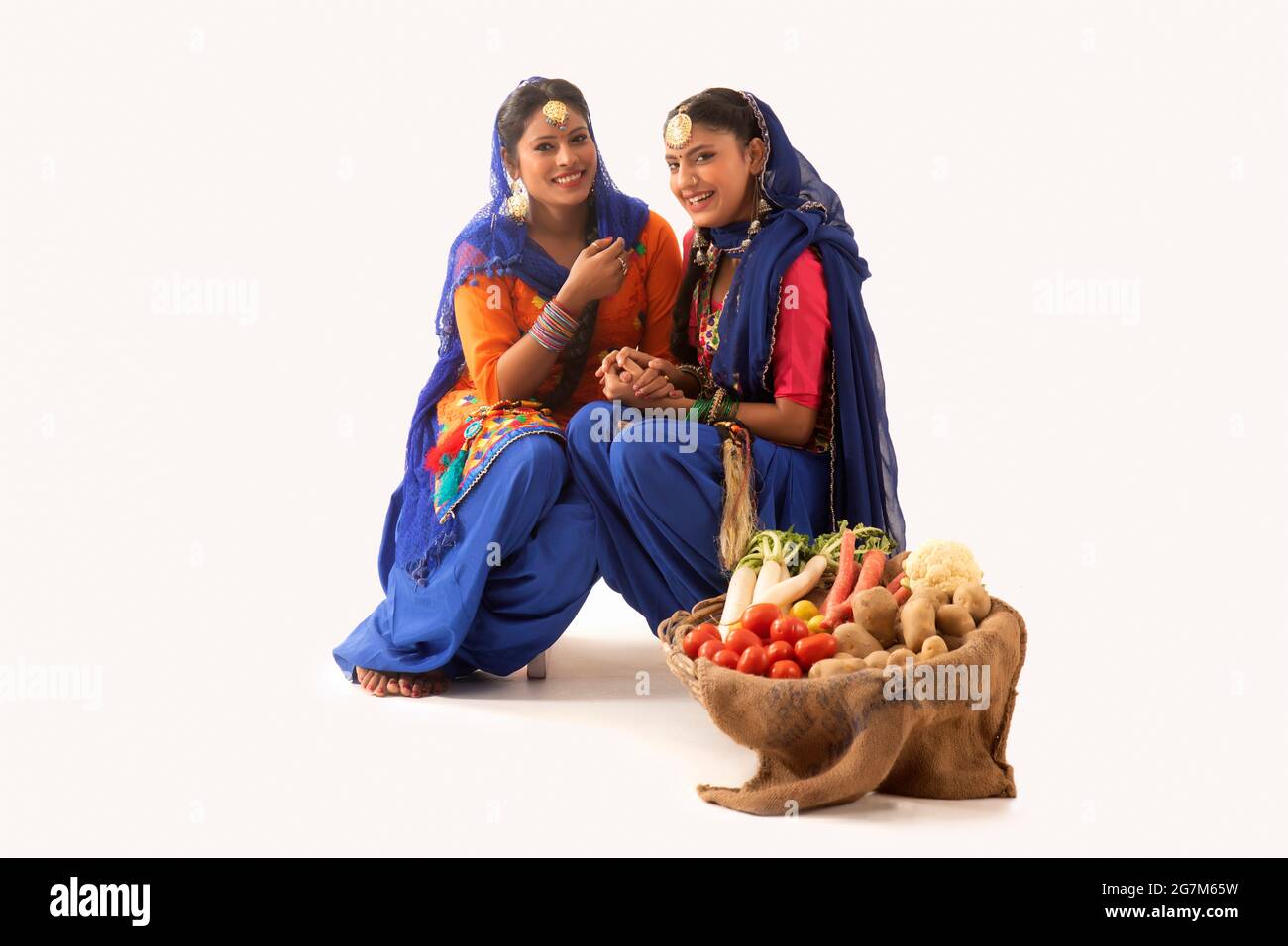 Due donne in costume Giddha seduti insieme con un cesto di verdure al loro fianco. Foto Stock