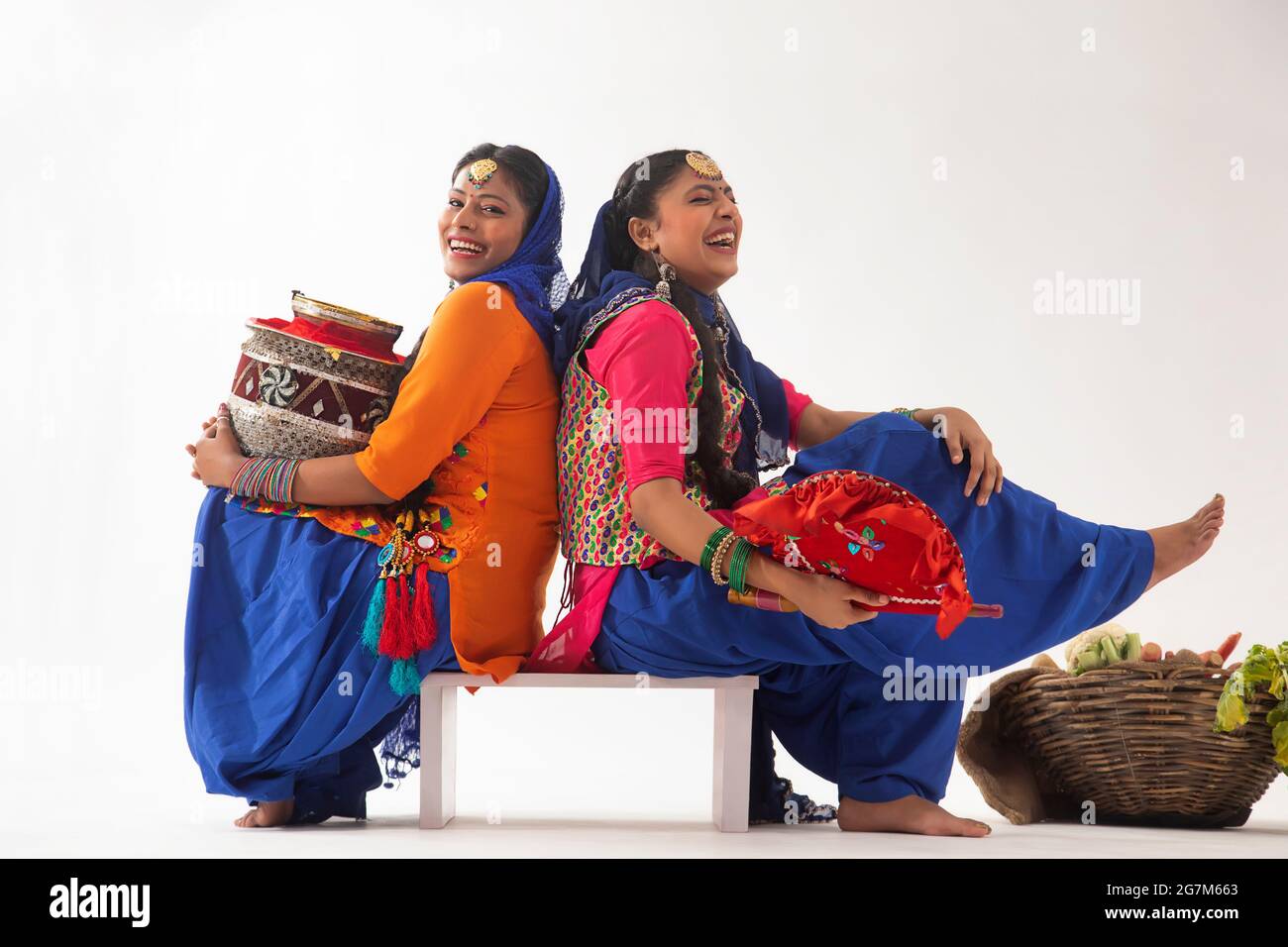 Due ballerini Giddha seduti con un ventilatore e un matki con un cesto di verdure dietro. Foto Stock
