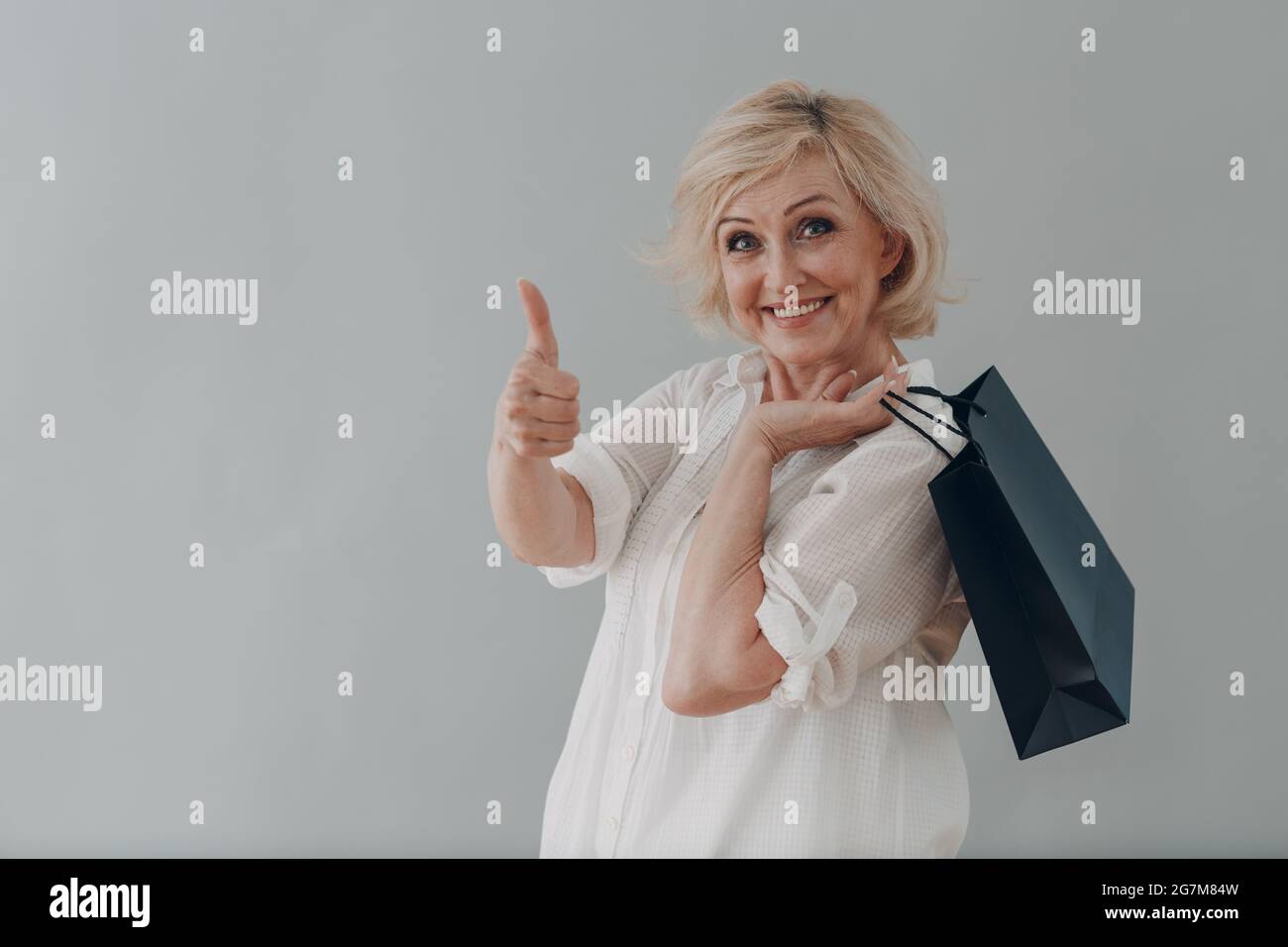 Anziana caucasica anziana donna anziana ritratto grigio capelli con borse per la spesa su sfondo grigio Foto Stock