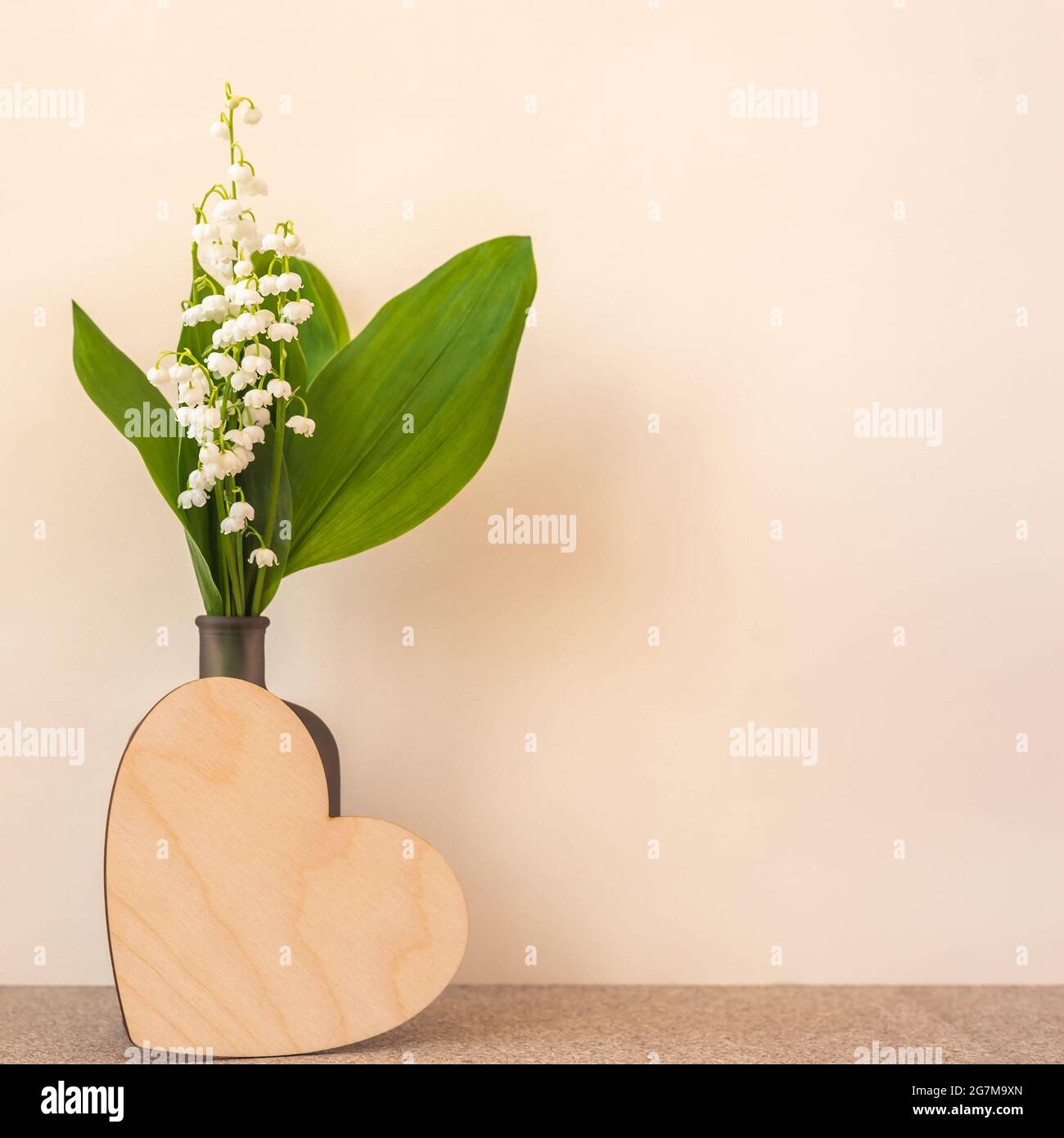Gigli della valle in bottiglia e cuore di legno sul beige Foto Stock