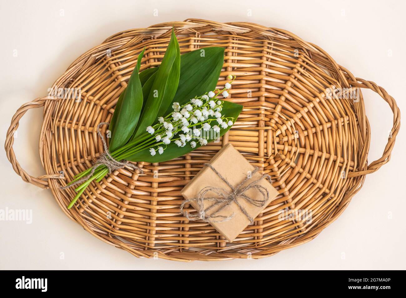 Vassoio con gigli della valle e scatola regalo su beige Foto Stock
