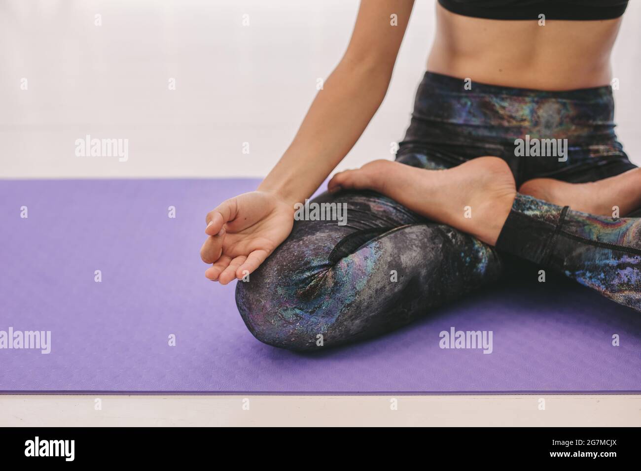 Donna in classe di yoga seduta sul tappeto da ginnastica con gambe incrociate e mano sul ginocchio. Meditazione femminile in Padmasana yoga posa in classe. Scatto ritagliato con f Foto Stock
