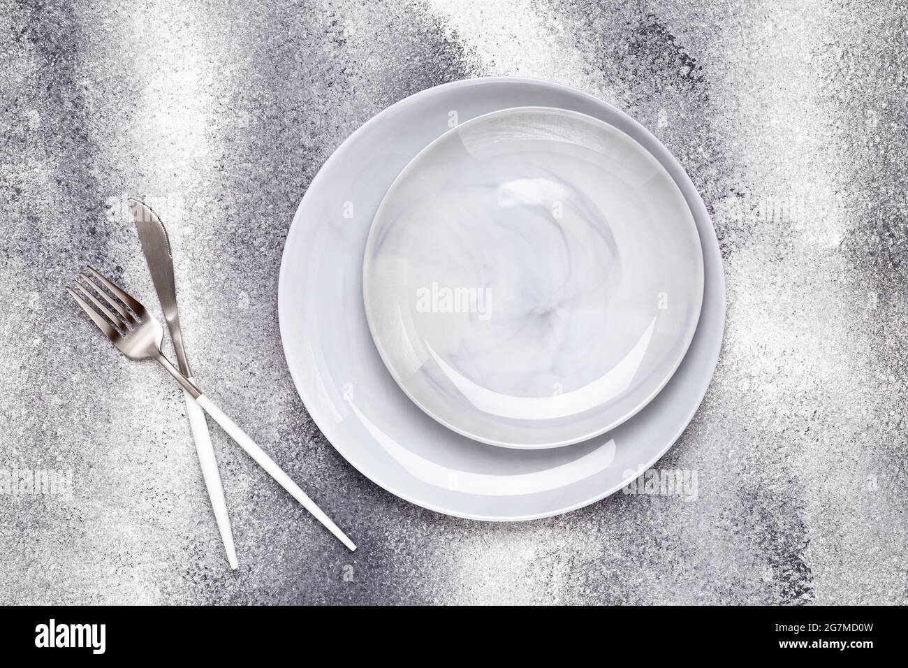 Piastra vuota in ceramica e coltello inutilizzato con forchetta, posate su tavola grigia, concetto di servizio. Design piatto. Menu del ristorante. Biglietto d'auguri, layout, mock Foto Stock