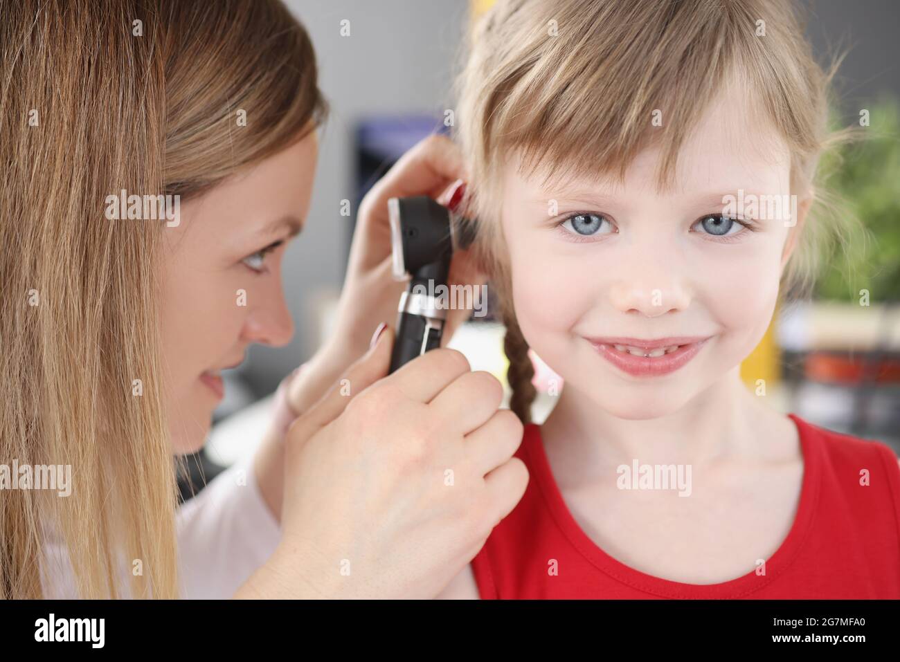 Donna pediatra che guarda il timpano di bambina usando otoscopio in clinica Foto Stock