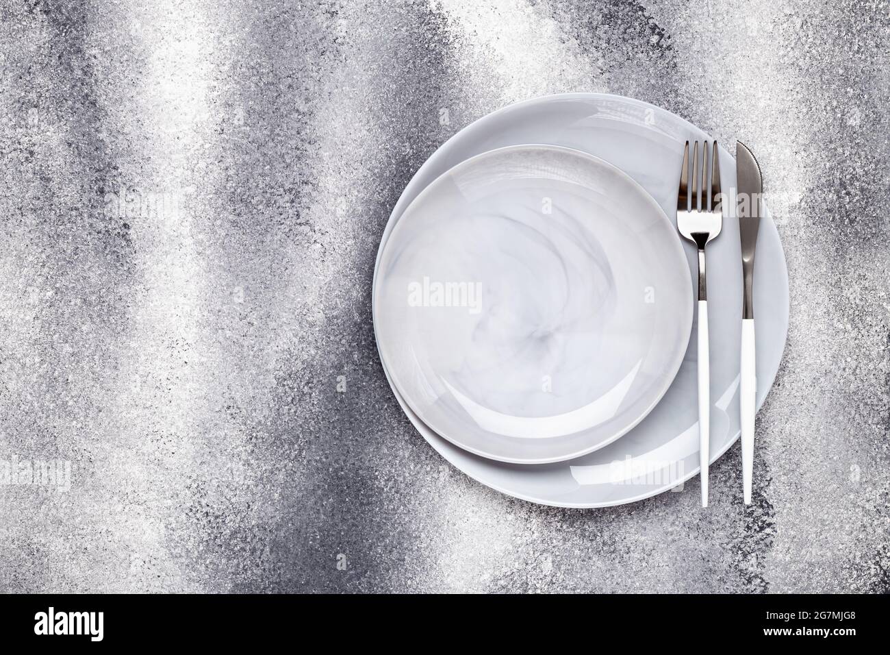 Due piastre vuote in ceramica e coltello inutilizzato con forchetta, stoviglie su un tavolo grigio a grunge, concetto di servizio. Design piatto. Menu caffetteria. Biglietto d'auguri, posa Foto Stock