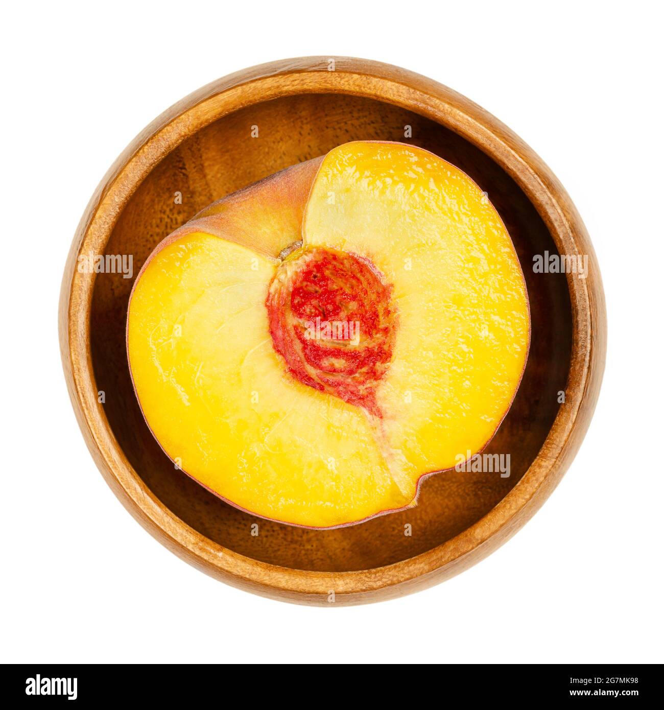 Pesche metà in una ciotola di legno. Sezione trasversale di un frutto maturo, con polpa di frutta gialla succosa, pietra arenaria rossa al centro e pelle vellutata. Foto Stock