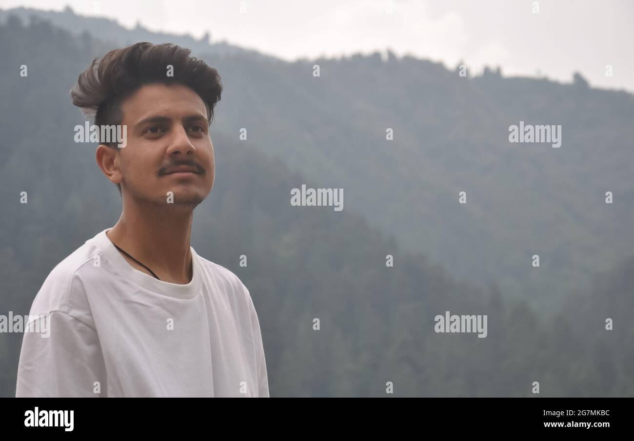 Foto di un giovane ragazzo con una t-shirt bianca che si trova all'esterno in zona collinare con spazio negativo Foto Stock