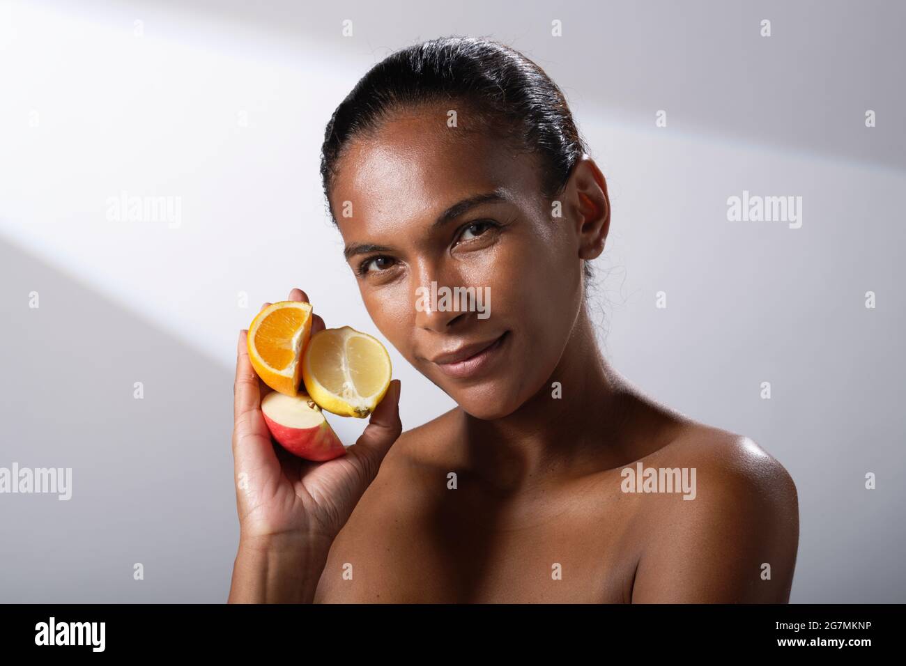 Immagini di bellezza di una donna con tonalità della pelle più scura. Immagini di testa e spalla di una signora. Sta tenendo una selezione di frutta. Mela, arancia e limone. Foto Stock