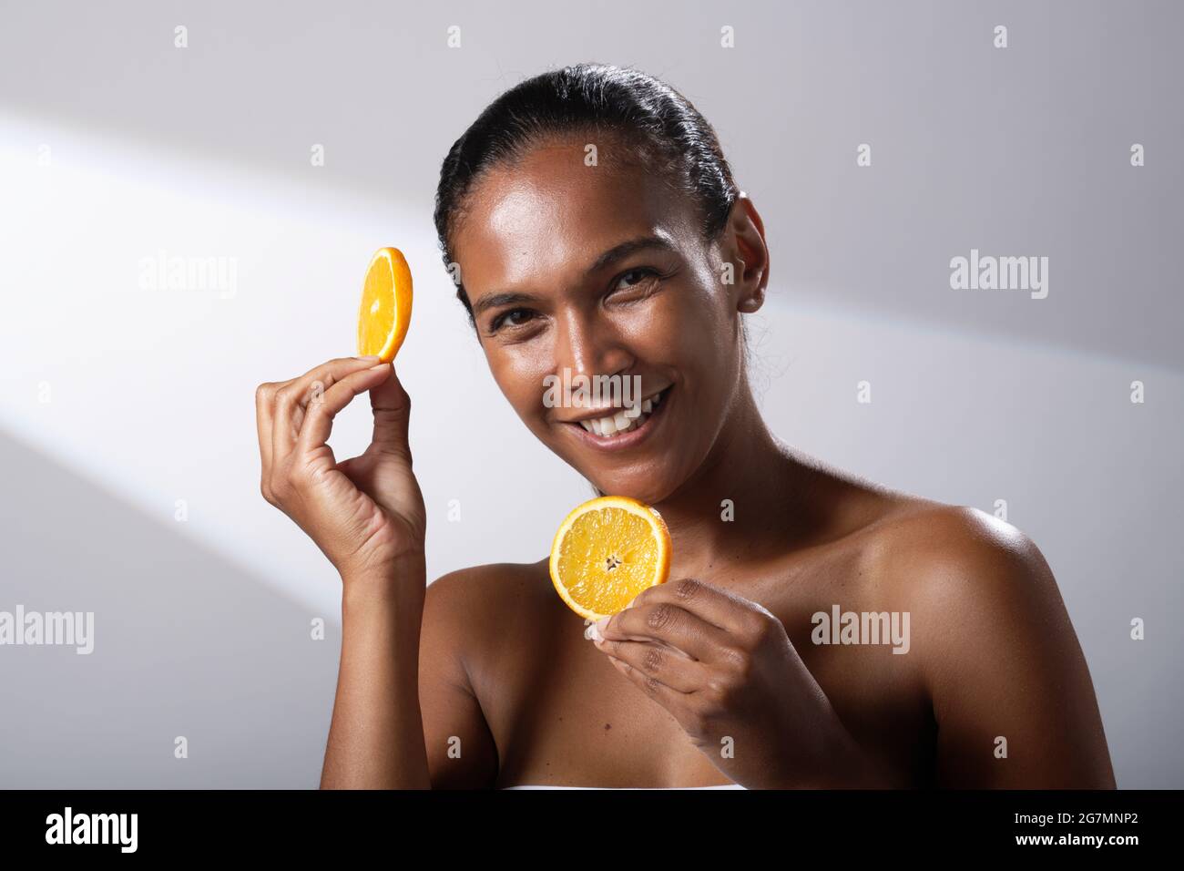 Immagini di bellezza di una donna con tonalità della pelle più scura. Foto di testa e spalla di sorridente, felice signora. Tenendo una fetta di frutta arancione. Foto Stock