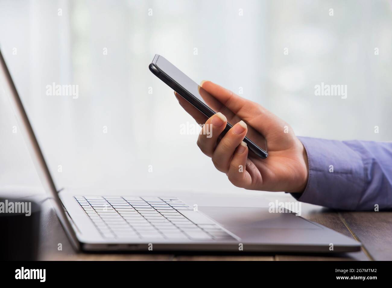 Mano umana che lavora sul telefono con un computer portatile davanti. Foto Stock