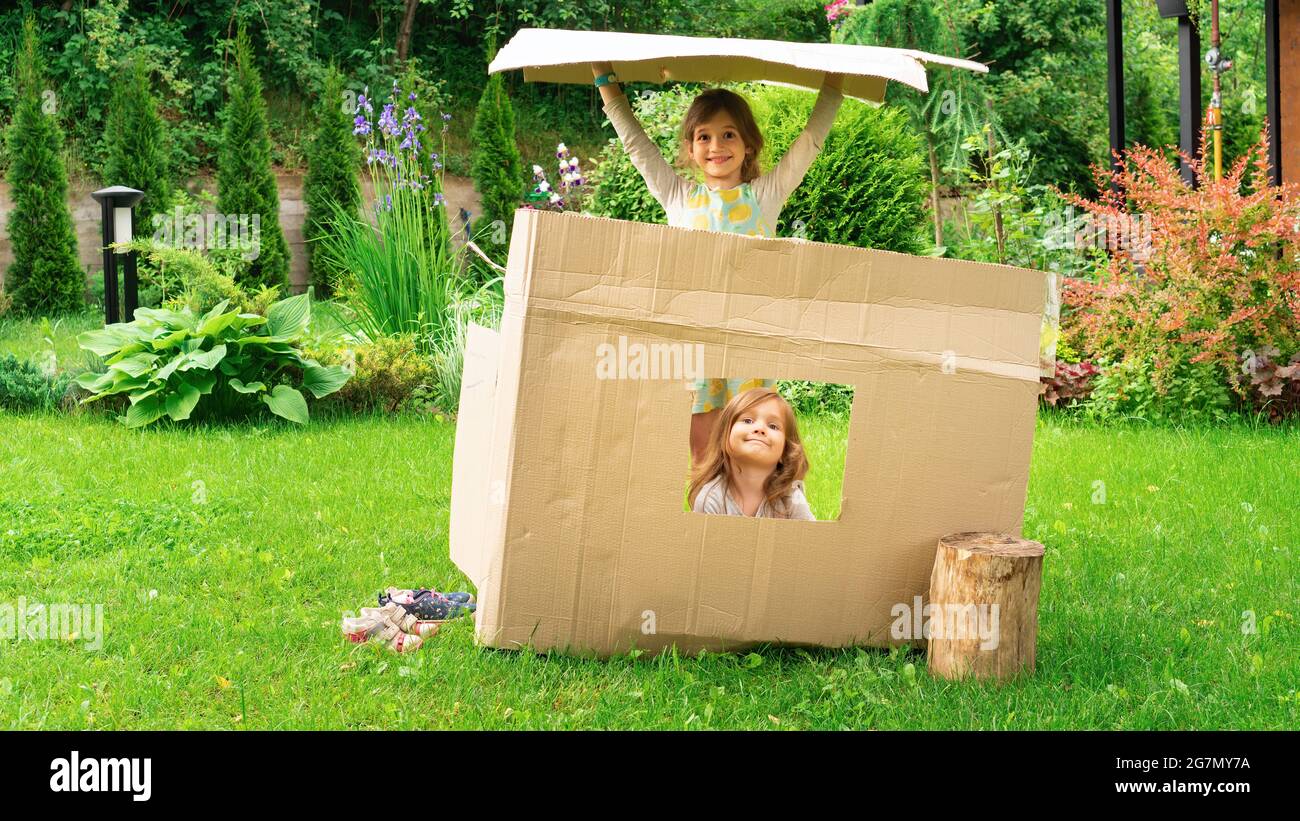 I bambini hanno costruito una casa di cartone fuori da una scatola e giocano in esso. Concetto di acquisto immobiliare. Passaggio a una nuova metafora domestica. Pubblicità per l'ostello. Foto Stock