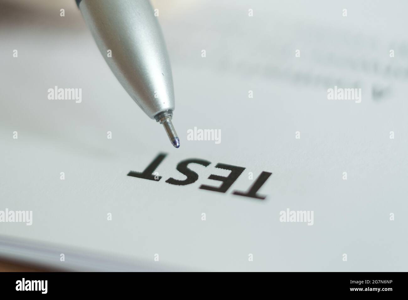 The word "Test" is written on a white sheet of paper, a pen is placed above the word. Blurred image. Foto Stock