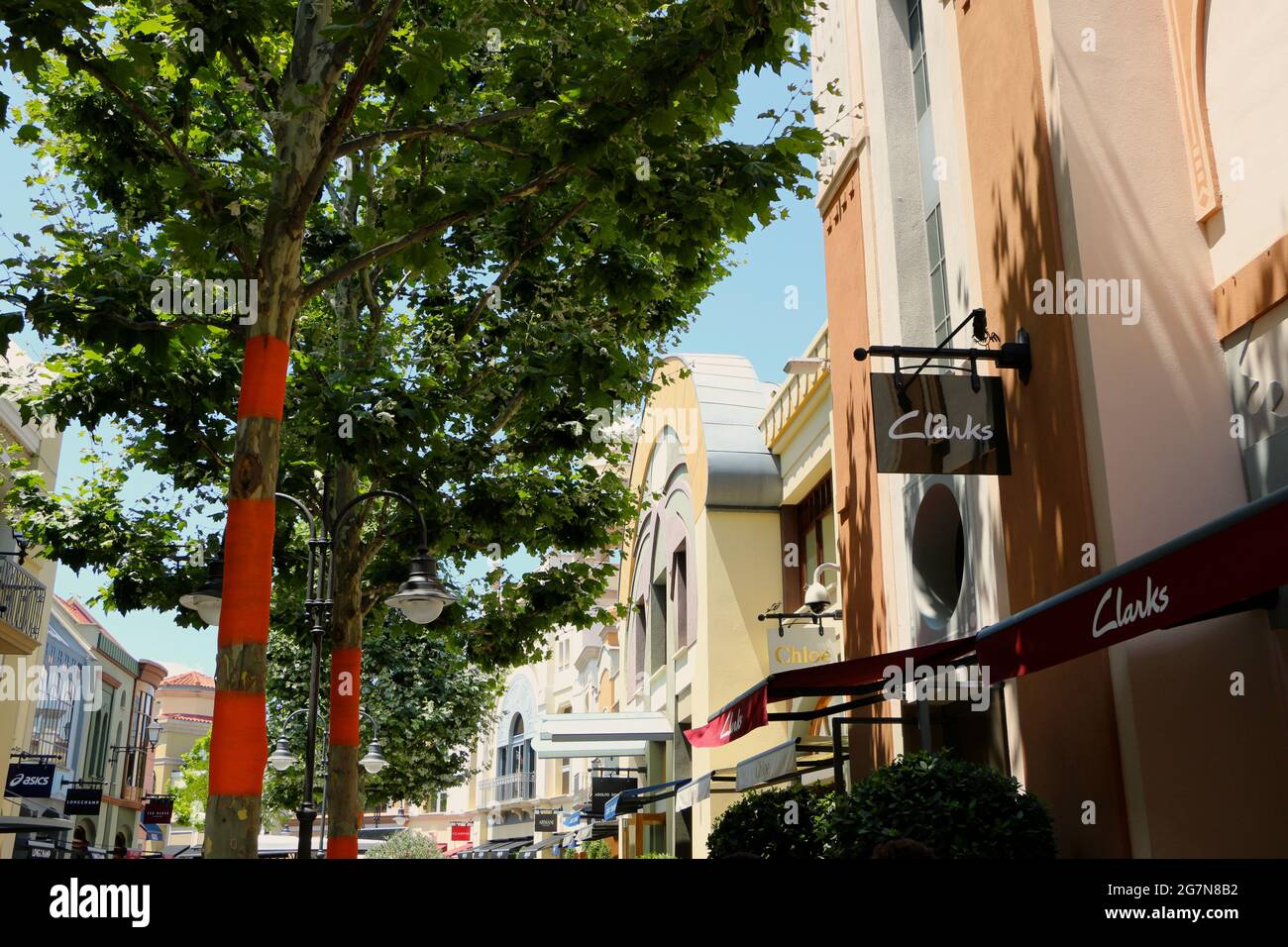 Las Rozas Outlets centro commerciale con un negozio di scarpe Clarks e fasce d'arancio sugli alberi per respingere gli insetti in un soleggiato pomeriggio estivo Madrid Spagna Foto Stock