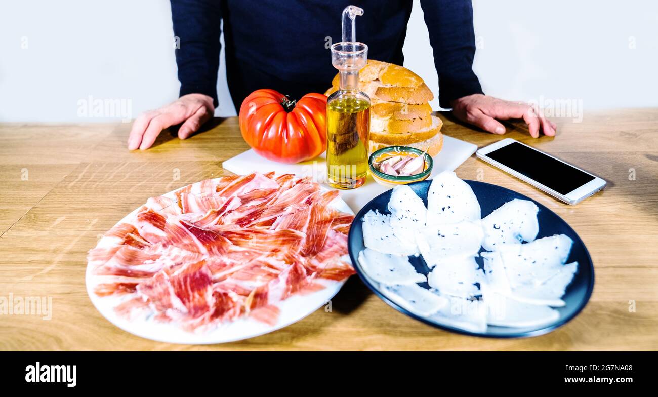 Anonimo persona che cucina un tipico catalano o cibo spagnolo. Pane con pomodoro, prosciutto iberico, formaggio di capra, olio d'oliva e aglio. Produ tradizionale Foto Stock