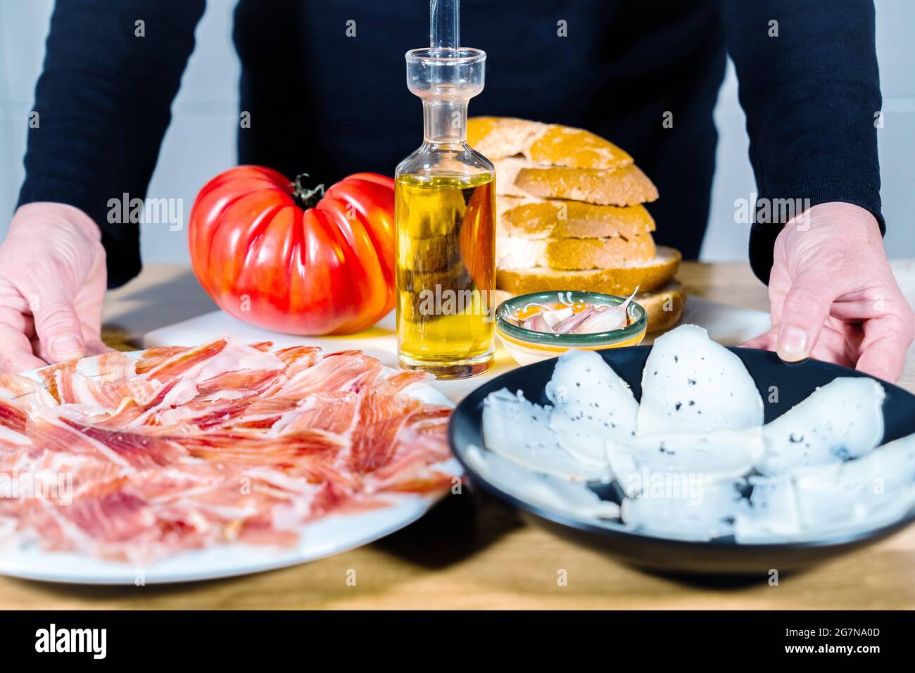 Cucina tipica spagnola o catalana su sfondo di legno. Prosciutto iberico, formaggio di capra, pane con pomodoro, vino rosso, olio e aglio. Preparazione di una cena o di un tocco Foto Stock
