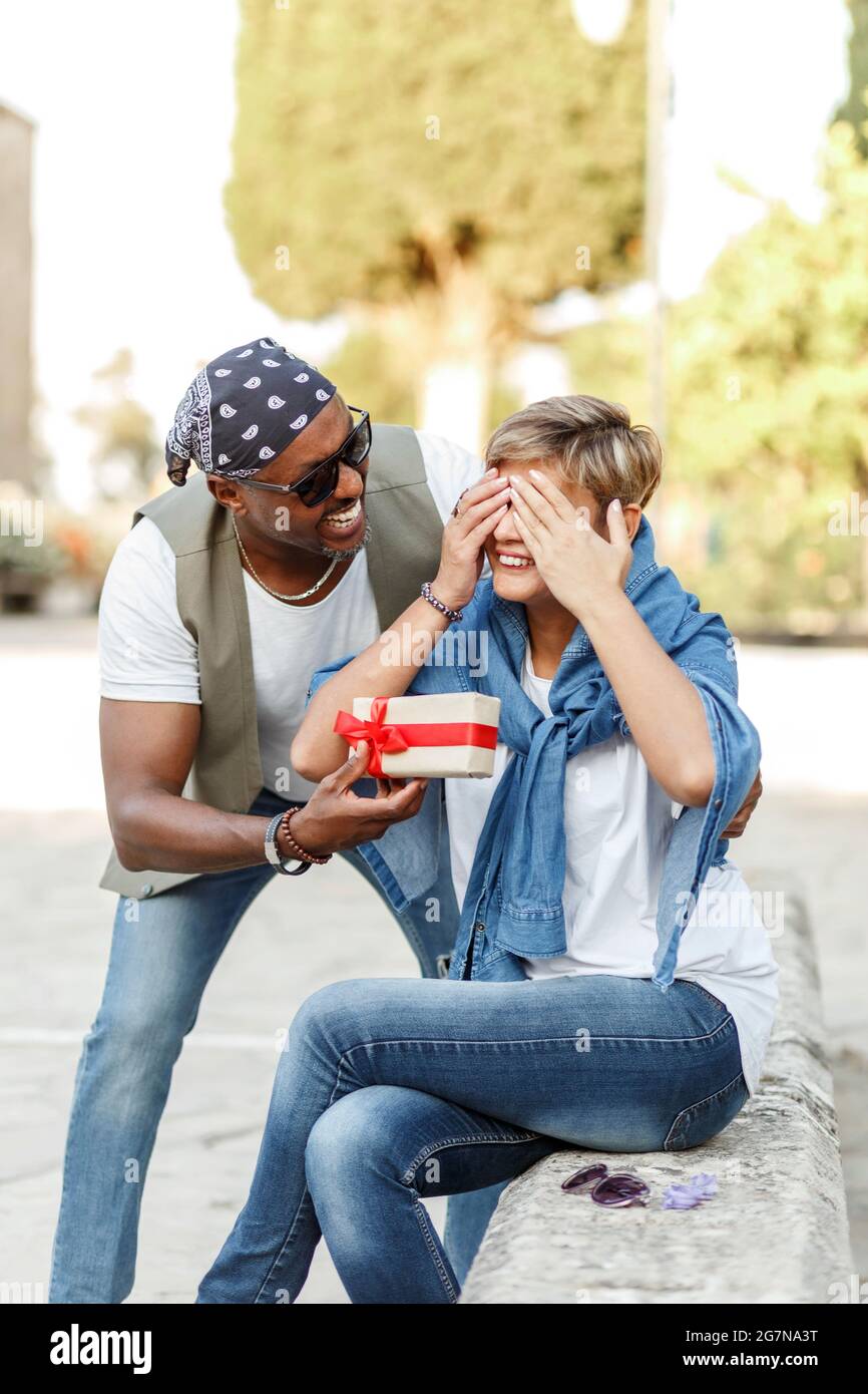 Felice coppia interracial di mezza età seduta . Uomo che dà il regalo di San Valentino alla sua donna, ragazza o moglie. Foto Stock