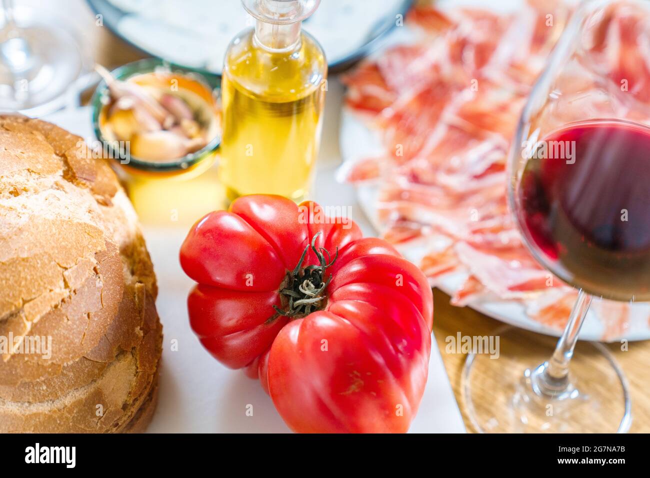 Piatti tipici catalani o spagnoli. Pane con pomodoro, prosciutto iberico, bicchiere di vino rosso, olio e aglio. Prodotti alimentari per la cena o tapas su una schiena di legno Foto Stock