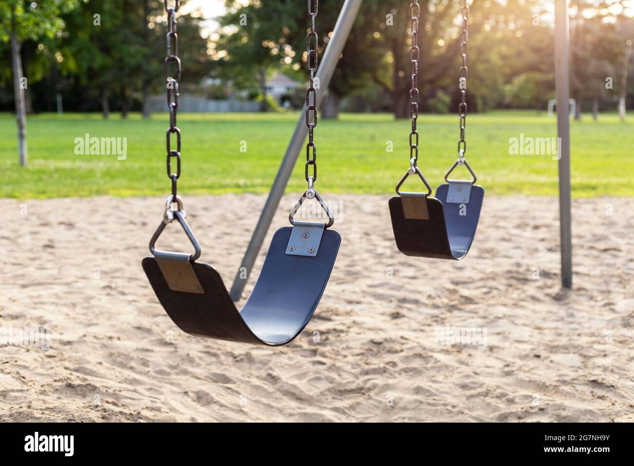 Parco giochi senza bambini nel parco pubblico locale, serie di altalene su  catene con sabbia sotto, erba, alberi e campo da calcio sullo sfondo in  Foto stock - Alamy