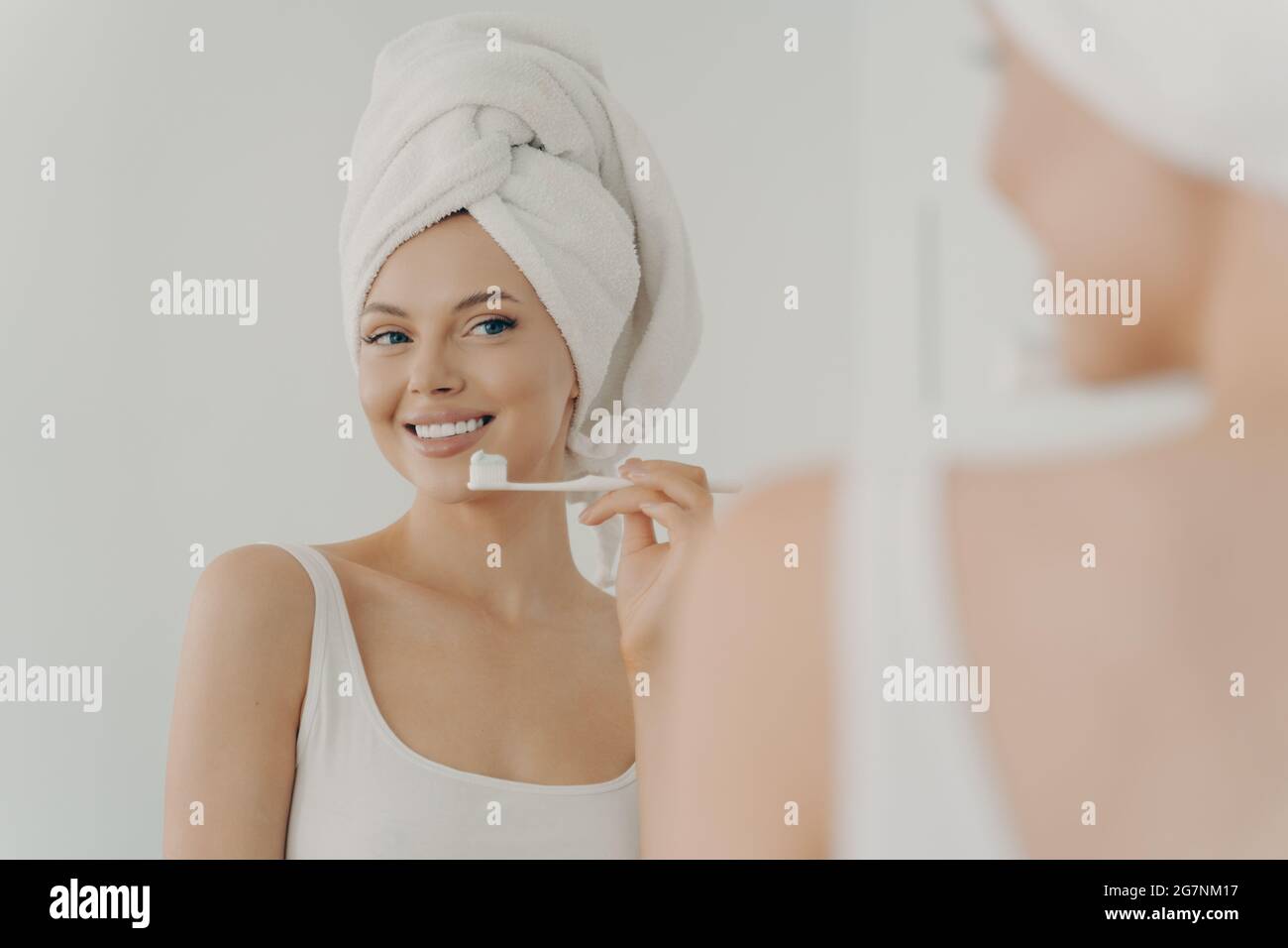 Bella giovane donna con un sorriso sano perfetto che spazzolava i denti e guardando nello specchio Foto Stock