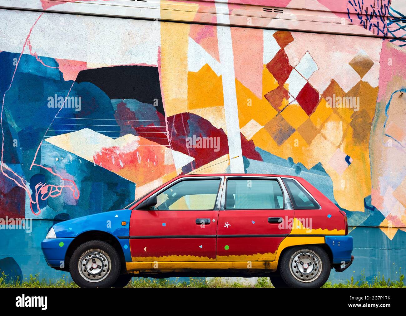 Una vecchia macchina dipinta sullo sfondo di una parete multicolore. Arte di strada Foto Stock
